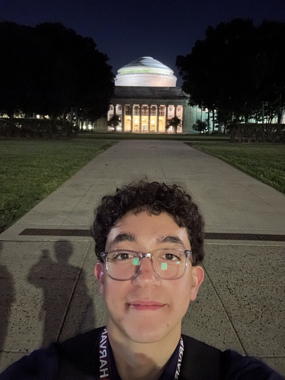 Yazan in front of the MIT dome at night, wearing a Harvard lanyard